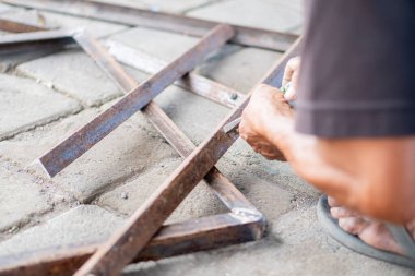 Beton bir yüzeyde metal çubuklarla çalışan bir insan ellerine ve metal parçalarına odaklanıyor..