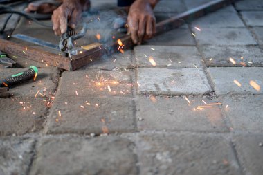 Asfaltlı yüzeyde cetvelle metal çerçeve ölçen biri. Kişi yalınayak ve dışarıda çalışıyor gibi görünüyor..