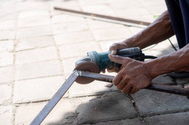Dışarıdaki asfalt yüzeyde metal kesmek için açı öğütücü kullanan biri..