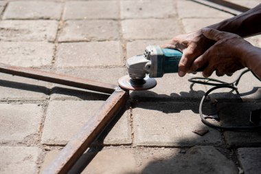Dışarıdaki asfalt yüzeyde metal kesmek için açı öğütücü kullanan biri..