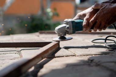 Açık havada metal bir çubuk kesmek için açı öğütücü kullanan biri. Kıvılcımlar uçuşuyor öğütme işleminden.