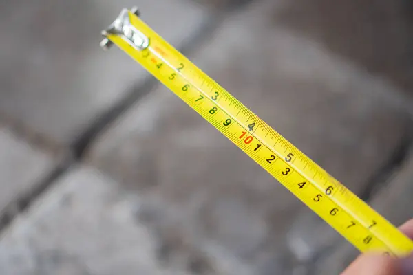 Gri tuğlaların bulanık arkaplanı boyunca uzanan sarı bir mezura yakın plan görüntüsü.