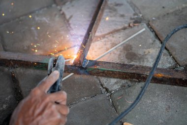 Metal çubukları kıvılcımlar ve gözle görülür dumanlar ile kaynak yapan birinin yakın çekimi.