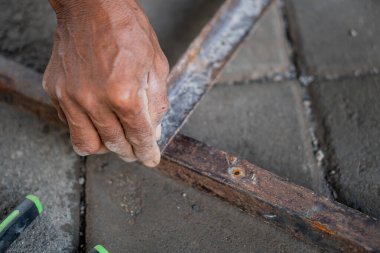 Paslı bir metal çerçeve üzerinde çalışan birinin elinin yakın çekimi, muhtemelen onarıyor ya da monte ediyor. El bir alet tutuyor ve metalde paslanma ve aşınma izleri var..