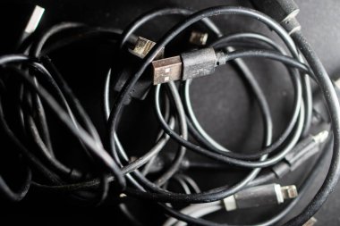 Arka planda bulanık bir klavye olan ve US B kablosu da dahil olmak üzere çeşitli kabloları birbirine dolanmış bir şekilde tutan bir elin yakın çekimi..