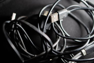 Arka planda bulanık bir klavye olan ve US B kablosu da dahil olmak üzere çeşitli kabloları birbirine dolanmış bir şekilde tutan bir elin yakın çekimi..