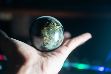 Arka planda el feneri olan parlak bir taş küreyi tutan bir el..