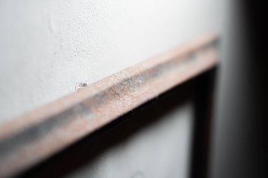 Paslı bir metal çerçeveyi beyaz bir duvara yakın çekim, sığ bir alan derinliği var..