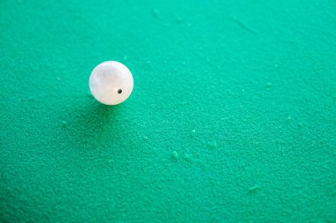 Yeşil desenli bir yüzeyde tek bir beyaz top, muhtemelen bir bilardo masası..