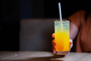 Tahta bir masada elinde pipetle bir bardak taze portakal suyu tutan bir adam..