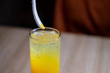 İçi ferahlatıcı portakal suyu, buz küpleri ve pipetle dolu bir bardağın yakın çekimi. Arka plan bulanık, içkiye odaklanmış..