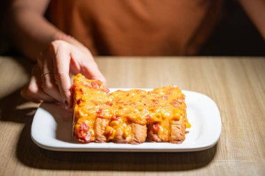 Beyaz bir tabakta dilimlenmiş domatesle kaplı peynirli ekmek tutan bir adam..