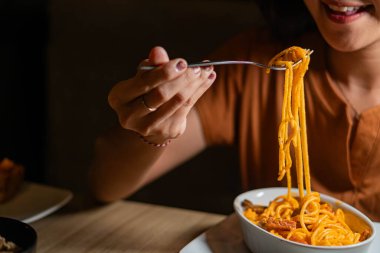 Beyaz bir tabaktan çatalla spagetti yiyen birinin yakın çekimi. Spagetti kremalı portakal sosuyla kaplı ve küçük et parçalarıyla süslenmiş..