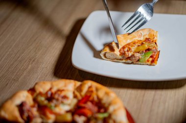 Kalın hamurlu taze pişmiş pizza. Üstünde dolma biber, sosis ve peynir gibi çeşitli malzemeler var. Tahta bir kürek üzerinde servis ediliyor..