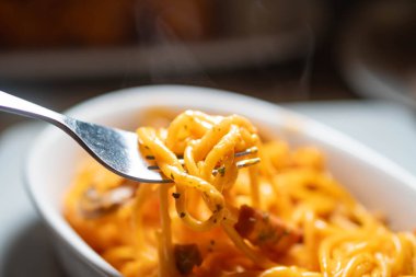 Domates soslu ve otlu spagettinin bir ısırığını tutan çatalın yakın çekimi, tabaktan buhar yükseliyor..