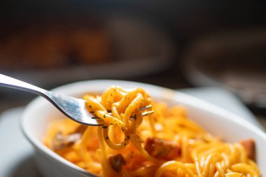 Domates soslu ve otlu spagettinin bir ısırığını tutan çatalın yakın çekimi, tabaktan buhar yükseliyor..