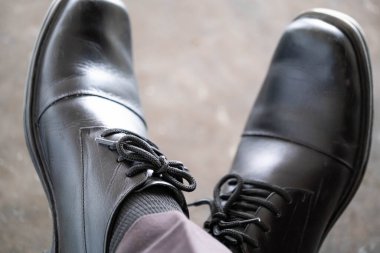 Siyah deri ayakkabılı, bağcıklı, bacak bacak üstüne atmış birinin yakın çekimi..