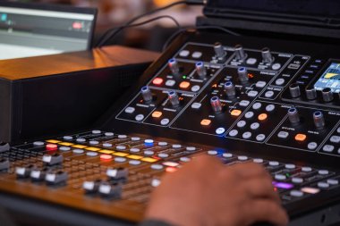 Profesyonel bir ses karıştırma konsolunu çeşitli düğmeler, düğmeler ve kaydırma çubuklarıyla çalıştıran kişinin yakın plan görüntüsü.