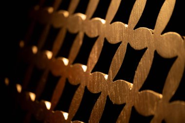 Altın kaplamalı dekoratif metal bir ızgaraya yakın plan, birbirine bağlı şekillerin yinelenen bir deseni, koyu arkaplana karşı dizilmiş.