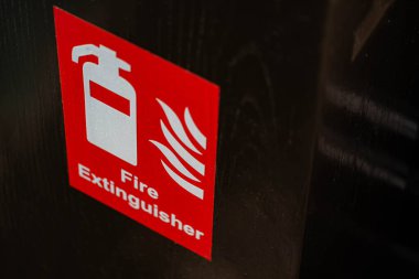 A close-up of a red fire extinguisher sign with white text and symbols on a dark background. clipart