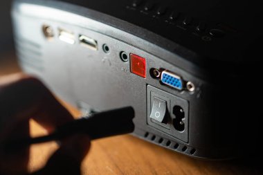 HUMID, VGA, ses ve güç anahtarı gibi çeşitli portları gösteren elektronik cihazın arka panelini kapat. Bir el limanların yanında bir kablo tutuyor..