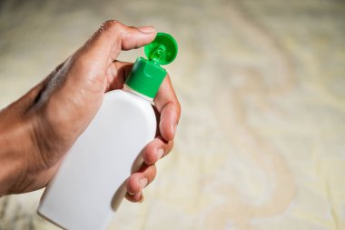 Yeşil kapaklı küçük beyaz plastik bir şişeyi tutan bir el. Sıvı dağıtıyor. Arka plan bulanık ve belirsiz..