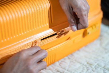 Turuncu bir bavulu yatağa bağlayan ellerin yakın çekimi..