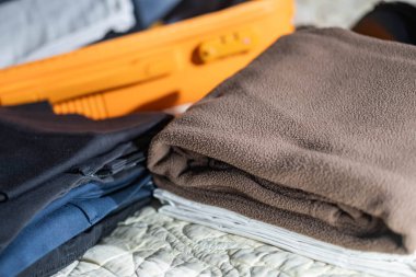 Düzgün katlanmış giysiler ve yatağın üzerinde turuncu bir bavul..