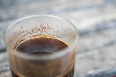 Kenarında koyu kahve ve kahve telvesi olan bir cam bardağa yakın plan, kırsal ahşap bir yüzeye yerleştirilmiş..