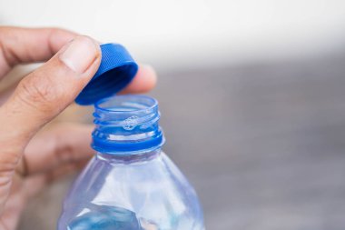 Mavi kapaklı plastik bir su şişesini açan elin yakın çekimi..