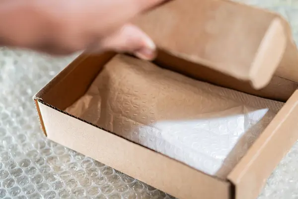 İçinde baloncuk ambalajı olan bir karton kutuyu açan kişi, baloncuk ambalaj kağıdına yerleştirilir.