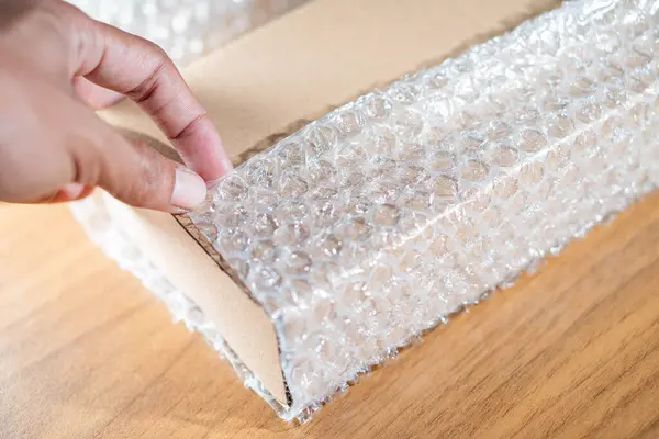 Tahta bir yüzeye baloncuk ambalajıyla karton bir kutuyu saran elin yakın çekimi.