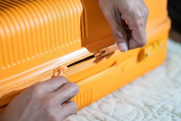 Turuncu bir bavulu yatağa bağlayan ellerin yakın çekimi..