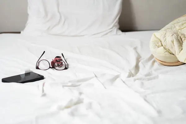 Bir gözlük, akıllı bir telefon ve beyaz bir yatağın üzerine sarılmış bir battaniye..