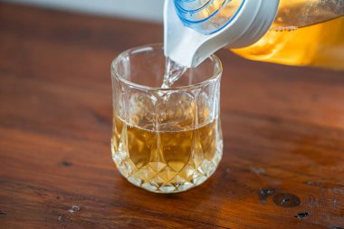 Tahta bir masadaki sürahide bulunan altın sıvıyla dolu bir bardak. Bardağın elmas deseni var ve sıvı ferahlatıcı görünüyor, muhtemelen buzlu çay ya da limonata..