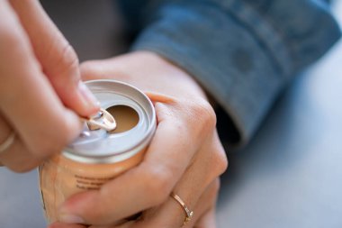 Bir insanın kola kutusunu açtığı yakın plan bir fotoğraf. Odak noktası, kot ceketin bulanık arka planına sahip parmaklarının sekmeyi çekmesi..