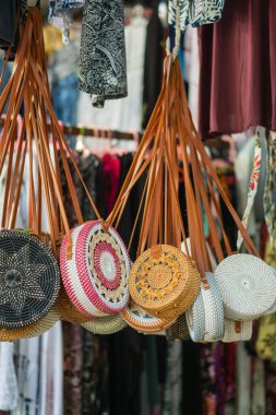 Markette asılı el yapımı, el yapımı, yuvarlak çantalar. Çantalar, arka planda çeşitli tekstil ürünleriyle çevrili karmaşık tasarımlar ve renkli desenler içeriyor..