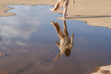 Islak bir yüzeyde yürüyen ve suda yansıma yaratan bir insan. Sahne, doğanın güzelliğini ve çevreyle insan etkileşimini yansıtıyor, sükunet ve hareket sergiliyor..