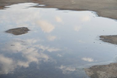Beton bir yüzeydeki su birikintisindeki bulutların sakin bir yansıması, doğada sakin bir an sergiliyor..