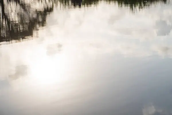 stock image A serene water surface reflecting clouds and sunlight, creating a tranquil and peaceful atmosphere. The image captures the beauty of nature with soft colors and gentle ripples.