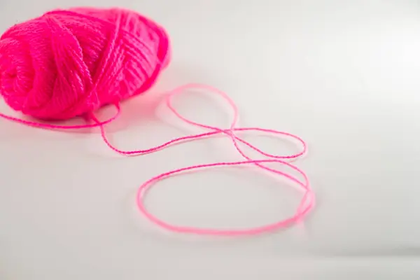 stock image A vibrant pink yarn ball with a loose strand forming a figure-eight shape on a white surface.