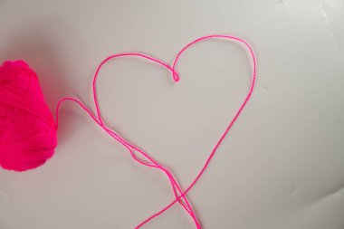 Aşkı ve yaratıcılığı sembolize eden, beyaz bir arka planda kalbe dönüşmüş canlı pembe bir iplik topu..