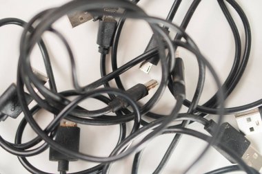 Beyaz arka planda birbirine dolanmış siyah US B kabloları ve konnektörleri.