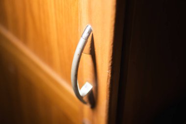 Ahşap bir dolaba metal bir kapı kolu yakın çekim, yumuşak ışıklandırma ahşap dokuyu ve sapı vurguluyor.