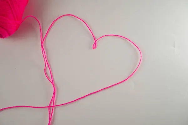 stock image A vibrant pink yarn ball with a strand shaped into a heart on a white background, symbolizing love and creativity.