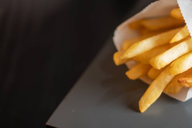 Kese kağıdında, koyu bir yüzeye yerleştirilmiş altın patates kızartmasının yakın çekimi. Patatesler çıtır çıtır ve taze pişmiş, yumuşak odaklı arka planı var..