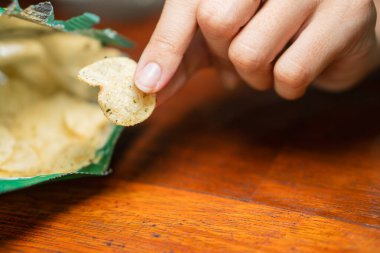 Tahta bir yüzeye dökülmüş patates cipsi torbası. Çipler açık renkli ve hafif benekli..