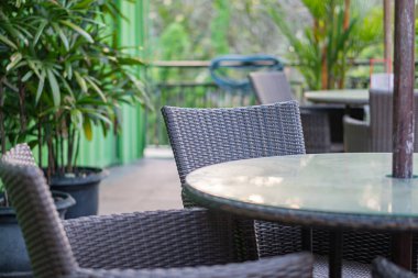 Hasır sandalyelerle çevrili yuvarlak cam bir masa içeren rahat bir kafeterya. Arka planda yemyeşil bitkiler görülebiliyor, sakin bir atmosfer yaratıyorlar..