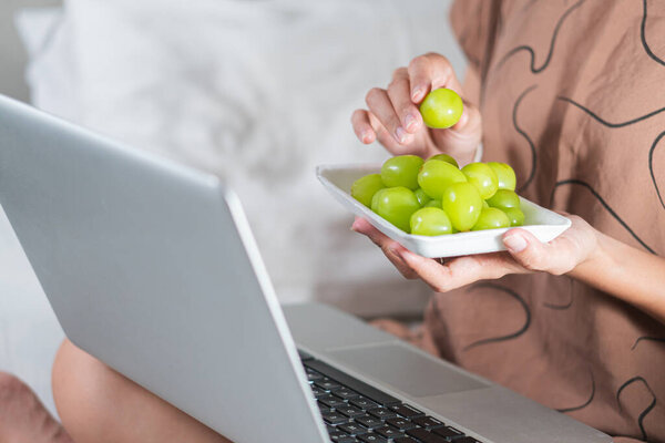 Крупный план руки, тянущейся за кучей зеленого винограда на белой тарелке. Внимание сосредоточено на пальцах, мягко прикасающихся к винограду, что подчеркивает его свежесть и цвет.