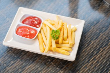 İki küçük kase ketçapla servis edilen, maydanozla süslenmiş bir tabak altın patates kızartması..